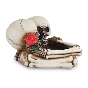 Posacenere gotico in resina con due teschi e una rosa rossa decorativa.