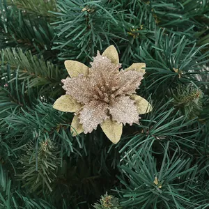 Detailed close-up of a glittering gold artificial Christmas flower on a pine tree branch.