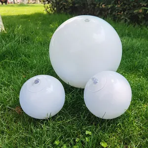 Set of three white PVC inflatable beach balls in different sizes on green grass.