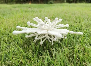 Detailed view of a white glittery 3D snowflake decoration resting on natural green grass.