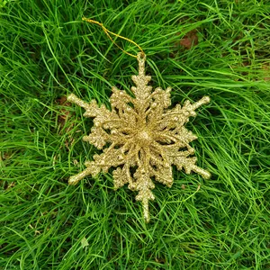Close-up of a 12cm gold glittery snowflake Christmas ornament lying on green grass.
