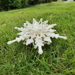 Macro detail of a 12cm white glittery 3D snowflake ornament on green grass backdrop