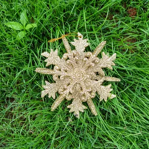 Macro detail of a 12cm gold glitter snowflake Christmas tree ornament hanging on grass.