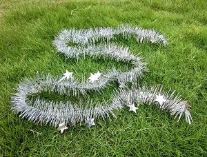 Detailed view of a 2m silver Christmas tinsel garland with star ornaments on grass