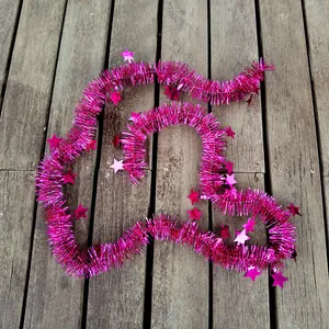 Pink Christmas star tinsel garland shown on rustic wooden floor planks for detail