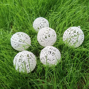 Six white hollowed-out snowflake Christmas balls with fine glitter on green grass