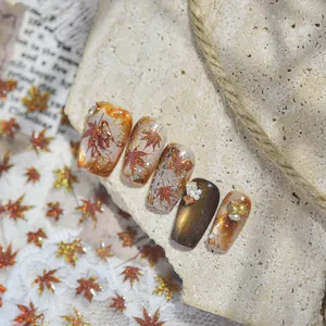 Detailed macro shot of autumn maple leaf nail stickers with gold glitter and pearls