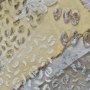 Macro view of metallic gold and white feather nail art stickers on wood background.