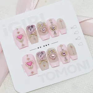 Détail d'ongles roses faits main haut de gamme avec cristaux en forme de cœur et nœuds