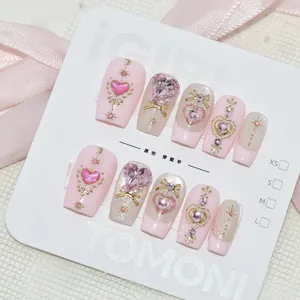 Détail de faux ongles faits à la main avec des gemmes en forme de cœur rose et des étoiles.