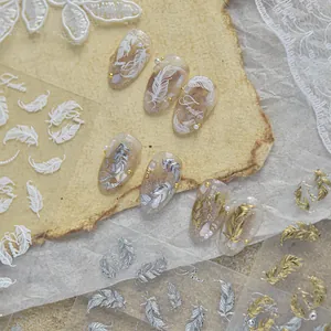 Close-up view of vintage metallic feather nail stickers in gold, silver, and white tones.