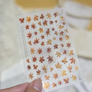 Close-up detail of metallic red-brown maple leaf nail art stickers with butterfly designs