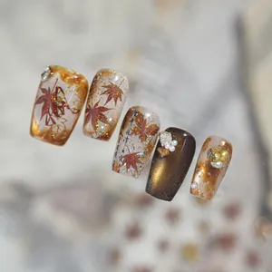 Close-up of autumn vintage nail stickers with red-brown maple leaf and gold foil detail