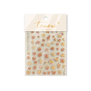 Detailed macro shot of vintage autumn maple leaf metallic nail art stickers in red and gold.