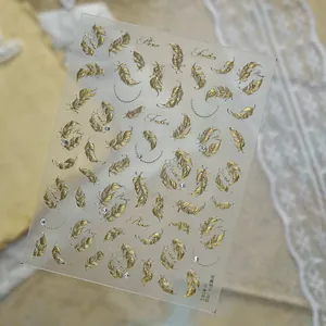 Detailed view of gold metallic feather nail stickers with shimmering rhinestone accents