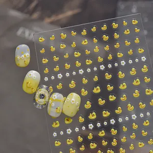 Gros plan détaillé d'autocollants 3D pour ongles motif canard jaune et fleurs.