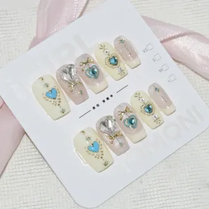 Magnifiques faux ongles faits main avec charms cœurs bleu clair et accents de papillons dorés.