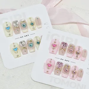 Vue macro détaillée de faux ongles faits main avec des gemmes en cœur et des dorures.