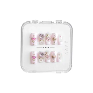 Vue détaillée de faux ongles faits main roses avec cristaux de cœur et nœuds dorés.