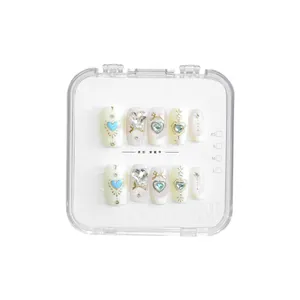 Faux ongles faits main style doux avec breloques cœur et nœud dans une boîte claire