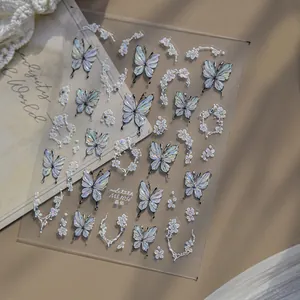 Detailed macro view of iridescent butterfly nail stickers with white floral motifs and crystal.