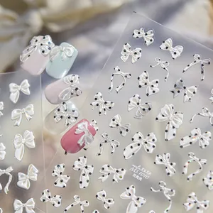 Primer plano de pegatinas de uñas 3D nacaradas con lazos y patrones de lunares negros