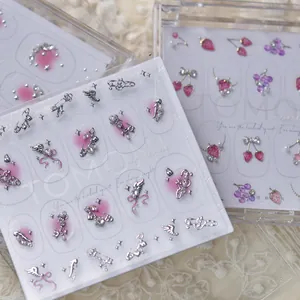 Vue détaillée de luxueux charms à ongles fraise et aile sur une carte d'affichage blanche.