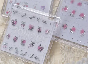Détail en gros plan des breloques à ongles de luxe Tomoni avec ailes argentées et accents roses