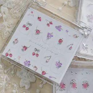 Gros plan détaillé de bijoux d'ongles en forme de fraises et de fruits dans un boîtier.