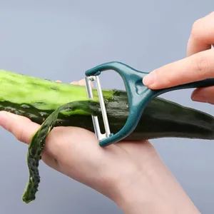 Stainless steel vegetable peeler with ergonomic green handle peeling fresh cucumber easily.