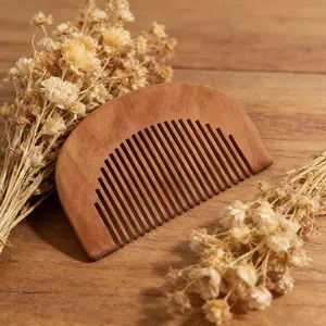 Closeup of a half-circle wooden comb placed on a rustic wooden table with dried flower decor.
