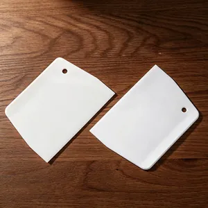Set of two white plastic dough scrapers with hanging holes for baking and kitchen prep work.