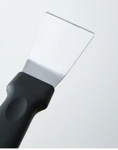 Détail de grattoir de cuisine en acier inoxydable lame et poignée noire en gros plan.