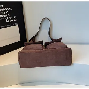 Detail shot of a dark brown suede shoulder bag featuring dual front flap pockets and texture.