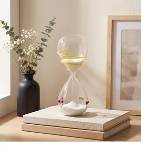Close-up of a glass sand timer with cherry patterns on a stack of beige books.