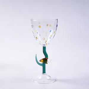 Creatief handbeschilderd wijnglas met stippen en een kleurrijk visfiguurtje op de steel.