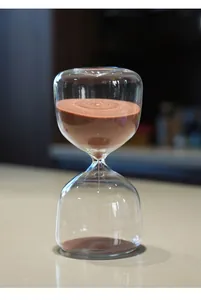 Vue détaillée d'un sablier rond en verre moderne avec du sable de couleur terre cuite