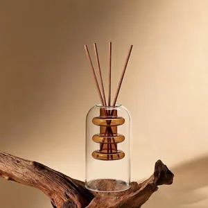 Minimalist double-layer glass reed diffuser bottle with amber core on wooden base.