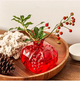 Detailed view of a mini pomegranate-shaped red glass vase on a wooden tray