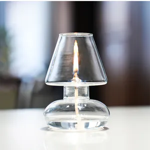 Close-up of a handmade glass oil lamp with a lit flame and transparent windproof shade.