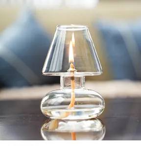 Handmade clear glass oil lamp with protective lampshade glowing on a dark reflective table