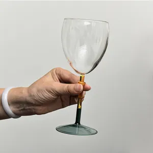 Elegant color-blocked stemmed wine glass held by hand against a neutral gray background