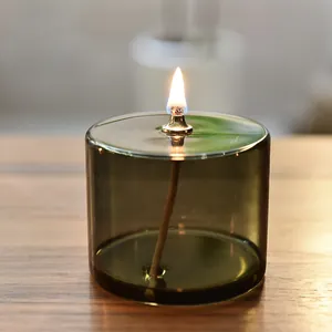 Elegante olivgrüne Glas-Öllampe mit brennender Flamme auf einem Holztisch