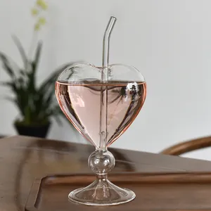 Elegant heart shaped glass cocktail cup with straw on a wooden tray