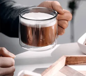Close-up of a double-walled glass mug with handle, filled with hot latte coffee.