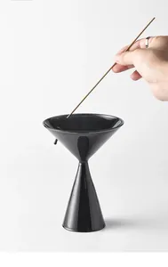 Close-up of hand placing a thin incense stick into a sleek black glass incense burner