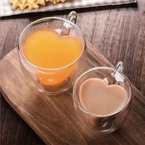Set of two heart-shaped double-walled glass cups filled with drinks on a wooden board