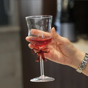 Elegant glass wine goblet featuring a red bow decoration on the stem held in hand