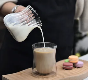 Close-up of pouring milk from a striated glass pitcher into a double-walled coffee cup