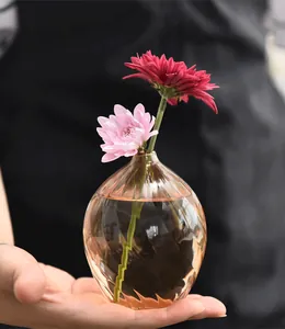 Detailed macro view of a champagne-colored glass bud vase being held in a hand